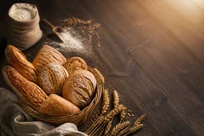 Pães artesanais rústicos numa cesta com farinha e trigo, luz quente de padaria