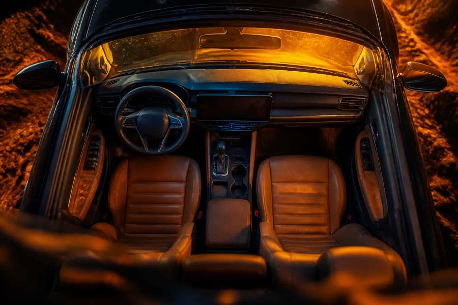 Interior de um SUV de aventura: cabine com bancos de couro caramelo, painel fosco, para-brisa e poeira dourada do cerrado ao entardecer