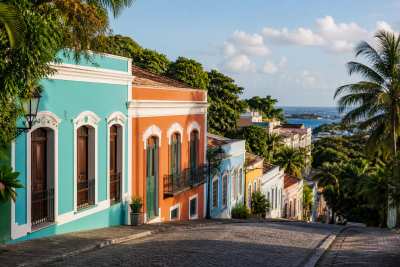 Ladeira de casario colonial colorido em encosta tropical, céu azul, composição vertical